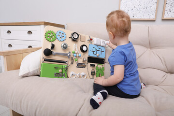 Cute little boy playing with busy board on sofa at home
