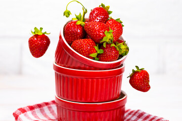 Juicy Fresh Strawberries in a Red Bowl on a piece of cloth on a white Brick background. Vitamin food. Copy space. Equilibrium floating food balance. Fruit Levitation.