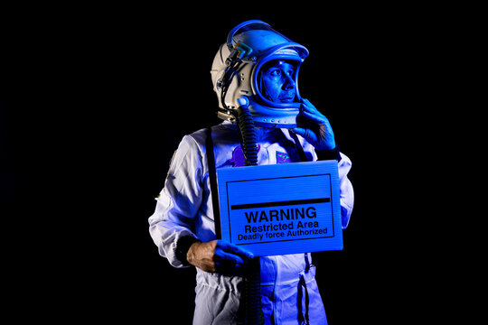 Serious astronaut in spacesuit showing placard with warning text
