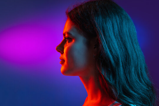 Caucasian young woman's portrait on dark studio background in neon. Concept of human emotions, facial expression.