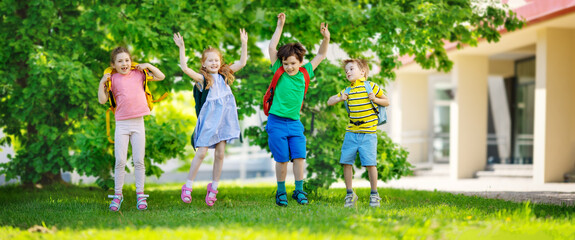 Cute children with rucksacks jumping and playing in the park near the school