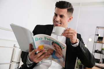 Man with cup reading magazine at table in office