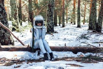 Anonymous female in space helmet sitting in snowy forest