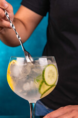 Bartender hand mixing CUCUMBER GIN FIZZ in foreground on ocean blue background.