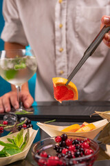 Bartender adding a slice of grapefruit in fruity cold tonic water having fresh ingredients in foreground.