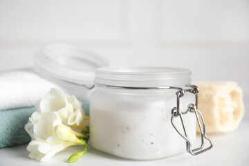 Jar of salt scrub, freesia flowers and towels on white table