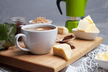 KETOGENIC KETO DIET DRINK. Coffee and cocoa mixed with ghee. Cup of bulletproof coffee with cocoa and ingredients on wooden background