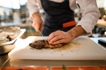 male chef cuts fried piece of meat on cutting board.