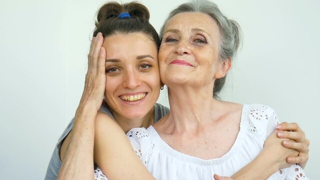Adult daughter is hugging her senior mother, the women are laughing together, sincere family of different age generations having fun on white background