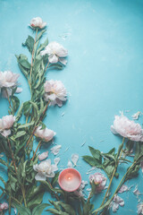 Blue background with pink pale peonies blooms , petals and burning candle . Top view