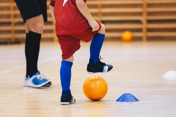 Boy in Soccer Clothes with Ornage Futsal Ball. Kid on indoor soccer training with coach. Child playing futsal on wooden floor. Futsal school practice with coach trainer