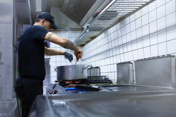 Young chef prepares grilled vegetables on cast iron griddle in his restaurant. Healthy food preparation concept.