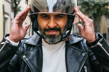 Smiling Hispanic biker putting on helmet on street