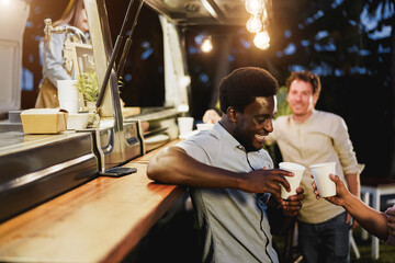 Multiracial people friends cheering with drinks in counter at food truck restaurant outdoor - Focus on african american man face