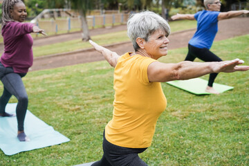 Senior people doing yoga class keeping distance at city park - Focus on center woman face