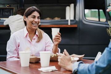 Multiracial people having fun eating and drinking outdoor at food truck restaurant - Focus on woman face