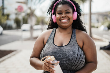 Sport curvy black girl listening music with headphones while doing workout outdoor - Focus on face