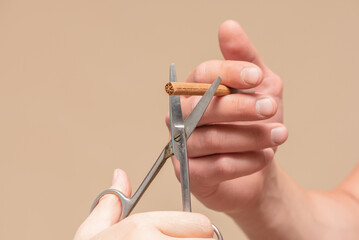 Male hand with a cigarette and woman hand with a scissors cuts a cigarette close up.