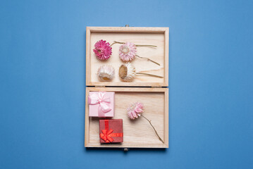 Open wooden giftbox with a small paper gift boxes and dried flowers within on the blue flat lay background.