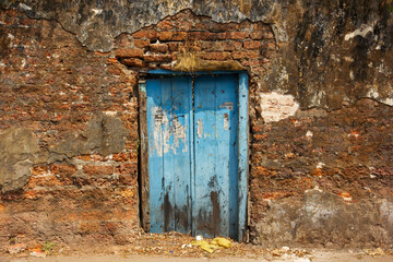 A rustic blue wooden door in an old, ruined laterite brick wall in the heritage town of Fort Kochi.