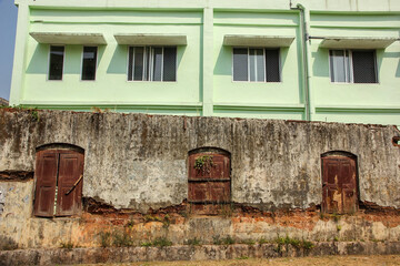 Vintage windows on rusty decaying brick wall with a modern concrete building behind in the heritage town of Mattancherry.