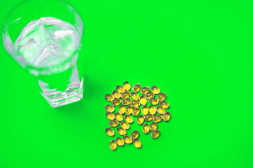Fish oil in capsules and a glass of water on a green background. The concept of a food supplement in the form of fish oil. Healthy Omega-3 Fatty Acids for the Cardiovascular System