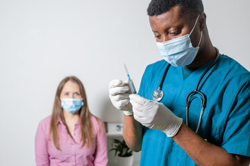 Doctor in medical mask holding syringe with medication