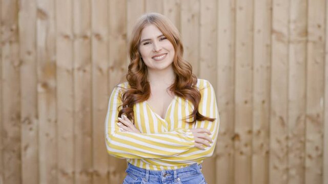 Confident woman standing in front of wooden wall with arms crossed