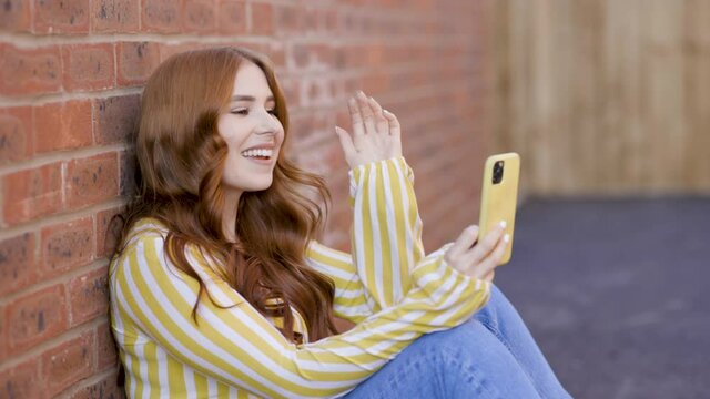 Smiling woman sitting in backyard having video call on smartphone