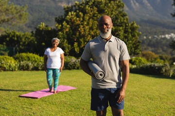 Portrait of smiling senior african american couple with yoga mat in countryside retreat