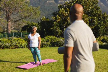 Portrait of smiling senior african american couple with yoga mat in countryside retreat - Powered by Adobe