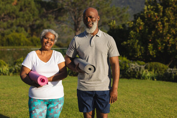 Portrait of smiling senior african american couple with yoga mat in countryside retreat