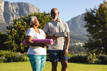 Portrait of smiling senior african american couple with yoga mat in countryside retreat