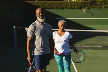 Tuinposter Portrait of smiling senior african american couple with tennis rackets on tennis court © wavebreak3