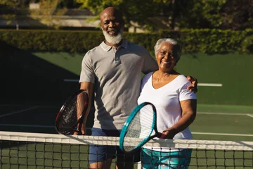Wandaufkleber Portrait of smiling senior african american couple with tennis rackets on tennis court © WavebreakMediaMicro