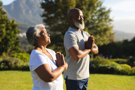 Senior african american couple meditating and practicing yoga with eyes closed in countryside - Powered by Adobe