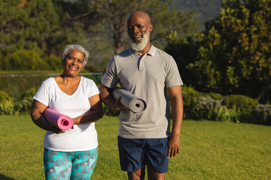 Portrait Of Smiling Senior African American Couple With Yoga Mat In Countryside Retreat