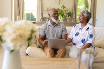 Senior african american couple sitting on sofa using laptop and smiling