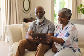 Senior african american couple sitting on sofa using tablet and smiling