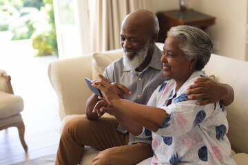 Senior african american couple sitting on sofa using smartphone taking selfies - Powered by Adobe