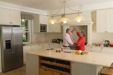Senior caucasian couple dancing together and smiling in kitchen