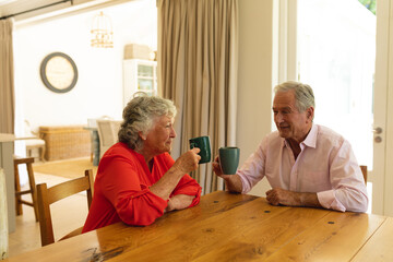 Senior caucasian couple sitting at table together drinking coffee in kitchen