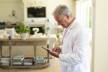 Fototapeta na wymiar Senior caucasian male doctor using tablet computer in living room