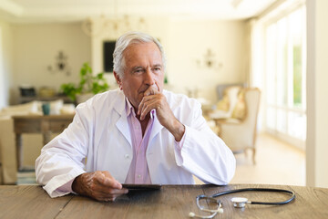 Senior caucasian male doctor sitting at table using tablet computer