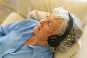 Senior caucasian woman sitting on sofa wearing headphones with eyes closed
