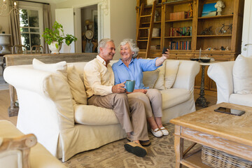 Senior caucasian couple sitting on sofa having video call using smartphone