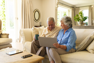 Obraz premium Senior caucasian couple sitting on sofa using laptop