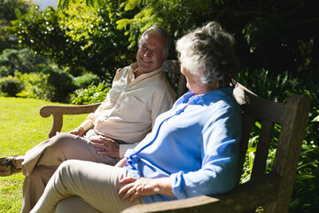 Senior caucasian couple sitting on bench together in sunny garden