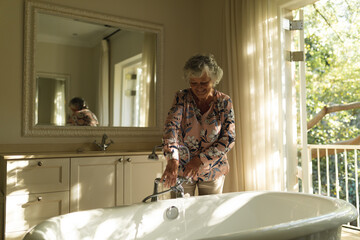 Senior caucasian woman running a bath in bathroom