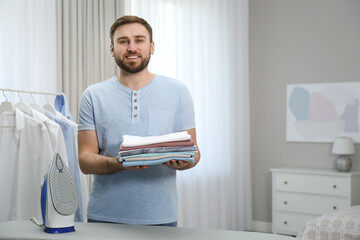 Man with folded clothes after ironing near board at home. Space for text